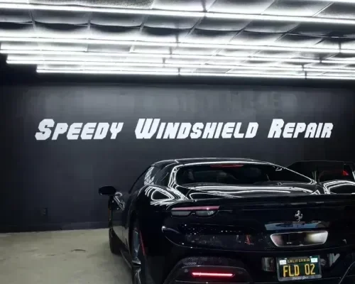 Black Ferrari in the Speedy Windshield Repair workshop bay beneath the wall sign