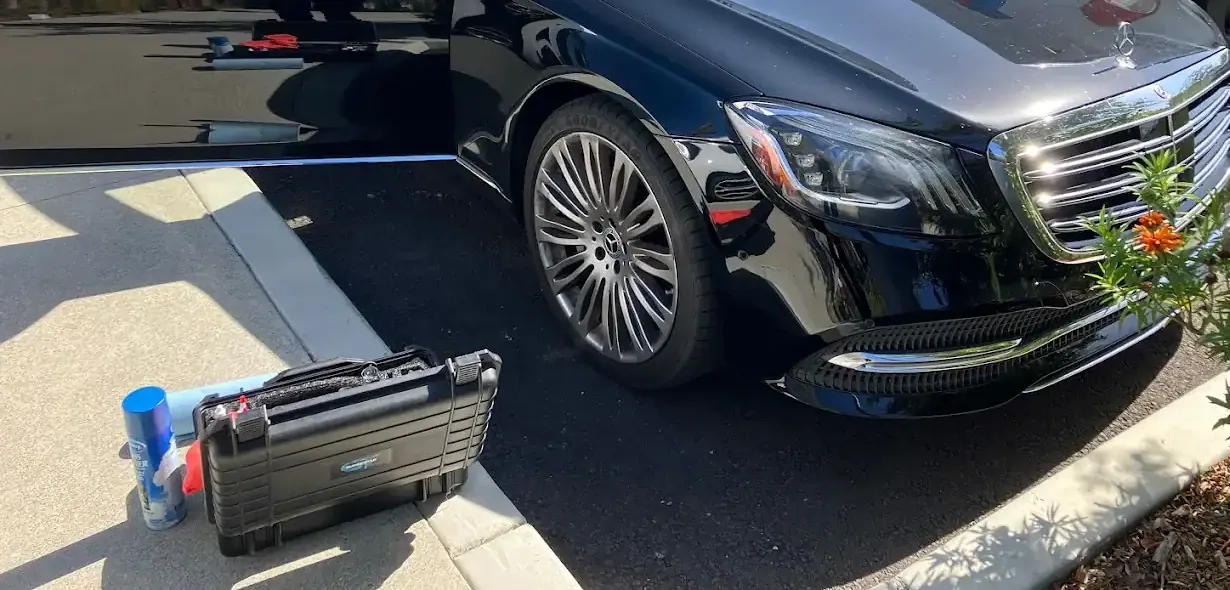Technician's tool case beside a black Mercedes sedan during a mobile windshield job on a residential driveway